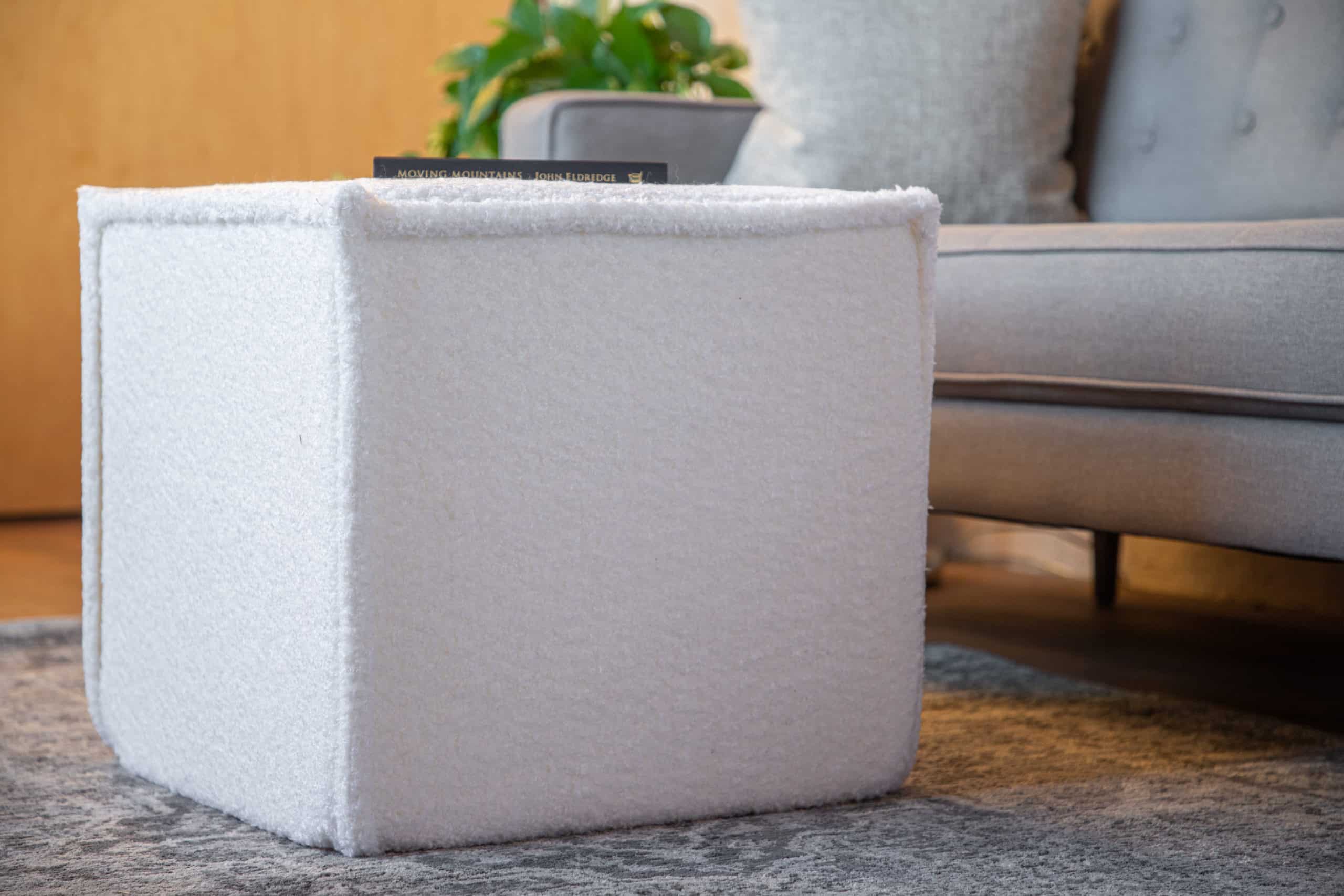 A Wovenbyrd Square Pouf in Cream accents a living room.